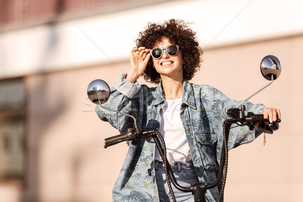 Image of pleased curly woman in sunglasses sitting on motorbike Stock photo © deandrobot