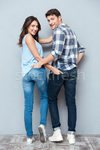 Couple standing backwards and looking at camera over gray background Stock photo © deandrobot