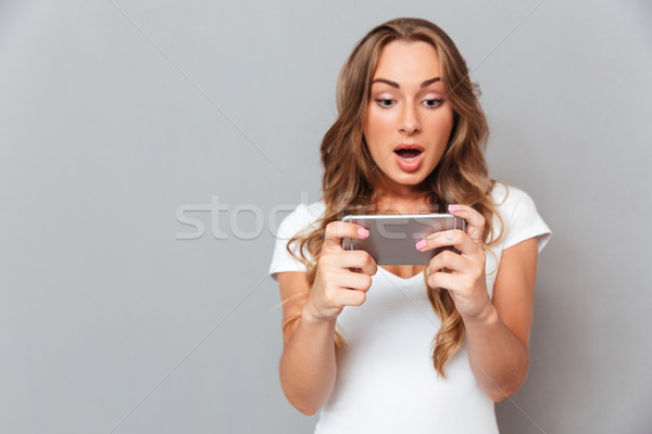 Surprised young woman looking on smartphone Stock photo © deandrobot