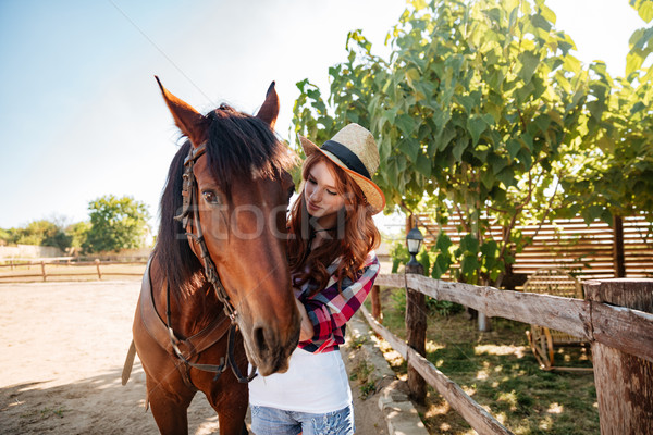 Stock photo: Redhead woman cowgirl taking care of her horse on farm