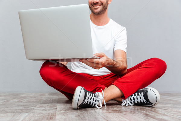 Happy smiling casual man sitting on the floor with laptop Stock photo © deandrobot