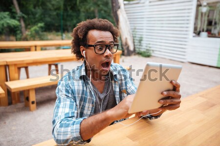 Stock photo: Smiling african man sitting and using tablet in outdoor cafe