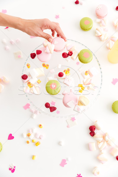 Top view of hand taking macaroon from plate with desserts Stock photo © deandrobot