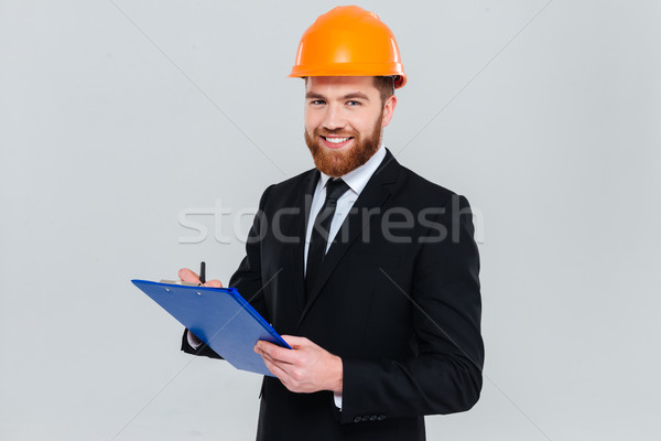 Sonriendo ingeniero portapapeles barbado traje casco Foto stock © deandrobot