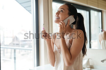 Woman using smartphone and brushing teeth in bathroom Stock photo © deandrobot