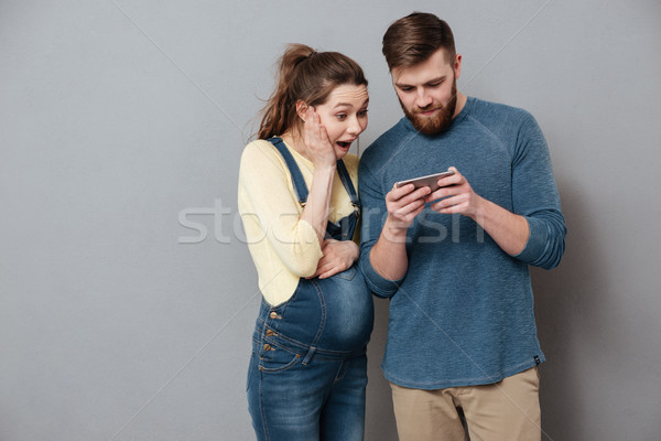 Young exciting couple looking together at mobile phone isolated Stock photo © deandrobot
