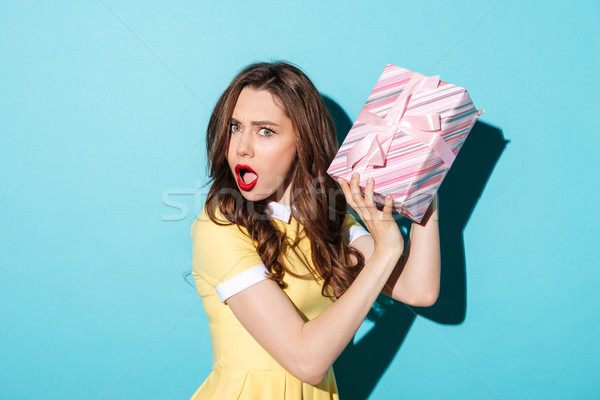 Portrait of an astonished girl in dress holding gift box Stock photo © deandrobot