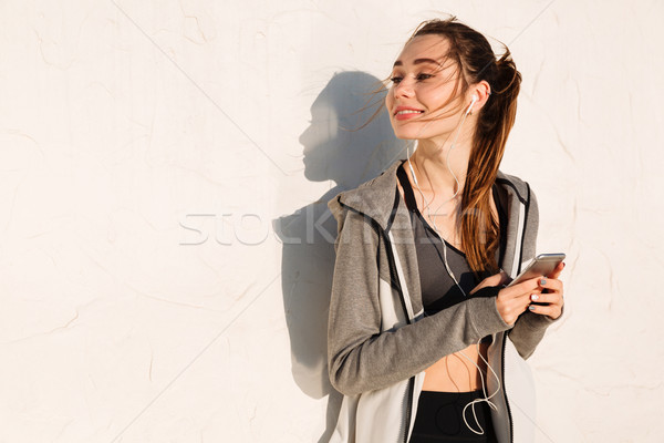 Shot of pretty smiling young sport woman holding smartphone, loo Stock photo © deandrobot