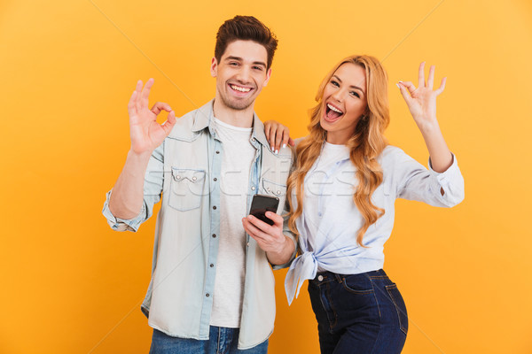 Photo of joyous couple man and woman smiling and showing ok sign Stock photo © deandrobot