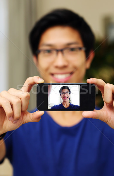 Smiling asian man taking self picture with smartphone camera. Focus on smartphone Stock photo © deandrobot