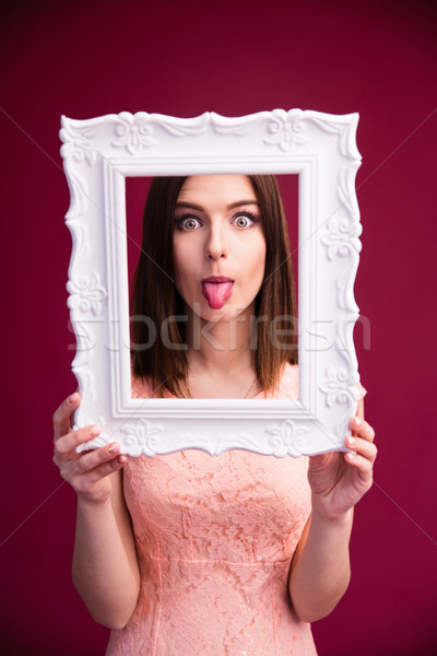 Woman showing her tongue and looking through frame Stock photo © deandrobot