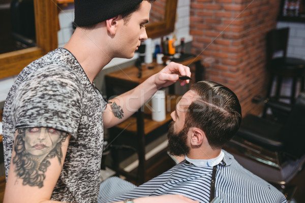 Young hairstylist combing hair of male client with comb Stock photo © deandrobot