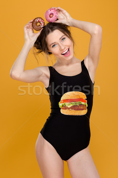 Cheerful amusing woman in swimsut holding donuts over her head  Stock photo © deandrobot