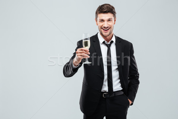Smiling young businesman with glass of champagne standing and celebrating Stock photo © deandrobot