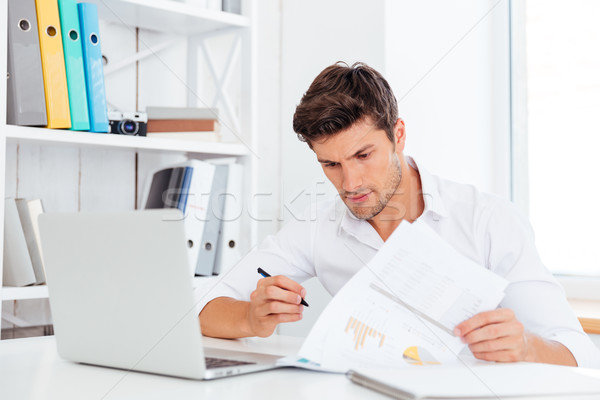Concentrated young businessman sitting and writing at the table Stock photo © deandrobot