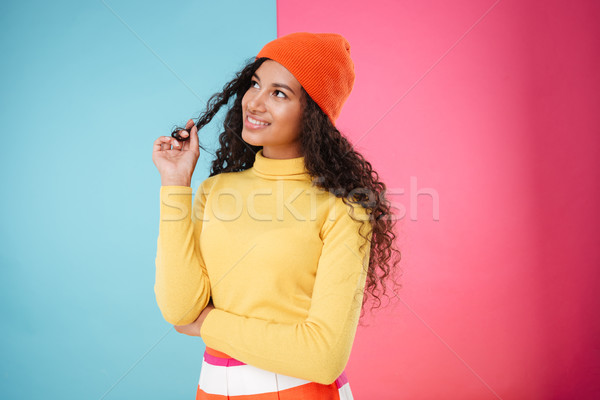 Smiling thoughtful african young woman in hat standing and thinking Stock photo © deandrobot