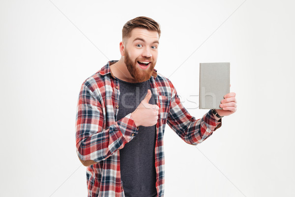 Man in plaid shirt holding book and showing thumb up Stock photo © deandrobot