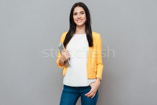 Young woman holding tablet computer over grey background. Stock photo © deandrobot
