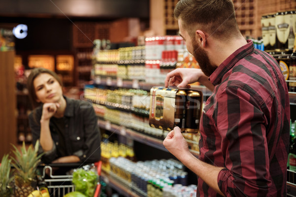 Loving couple in supermarket. Angry woman looking man holding beer. Stock photo © deandrobot