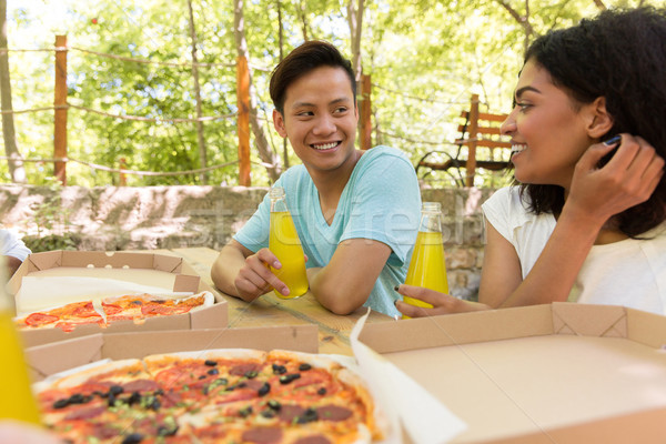Smiling young multiethnic friends students outdoors drinking juice eating pizza. Stock photo © deandrobot