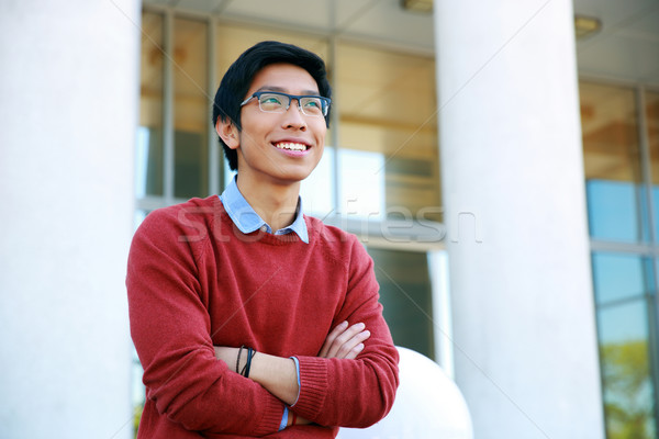 Portrait of a young happy asian man with arms folded looking up Stock photo © deandrobot