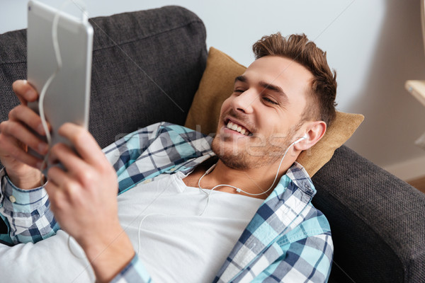 Cheerful bristle man using tablet computer while listening music Stock photo © deandrobot