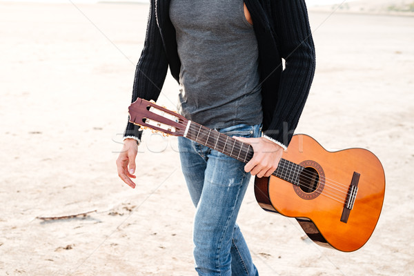 Casual man holding guitar and walking across seashore Stock photo © deandrobot