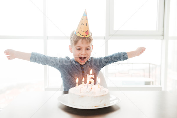 Birthday boy sitting in kitchen near cake while smiling Stock photo © deandrobot