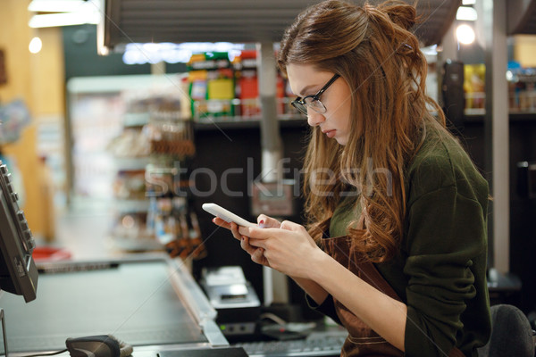 Cashier lady on workspace in supermarket shop using mobile Stock photo © deandrobot