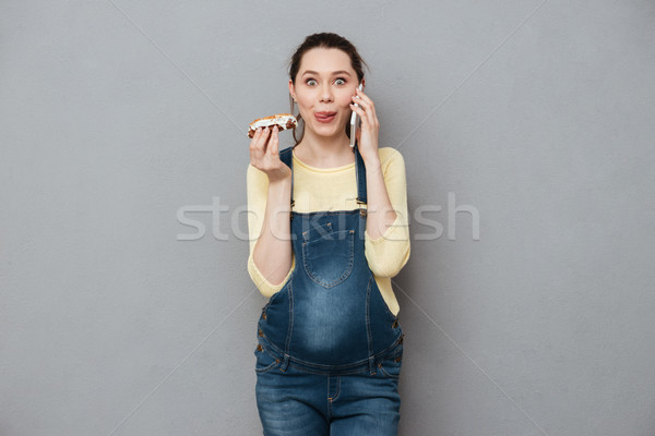 Pregnant hungry woman eating eclair and talking by phone. Stock photo © deandrobot