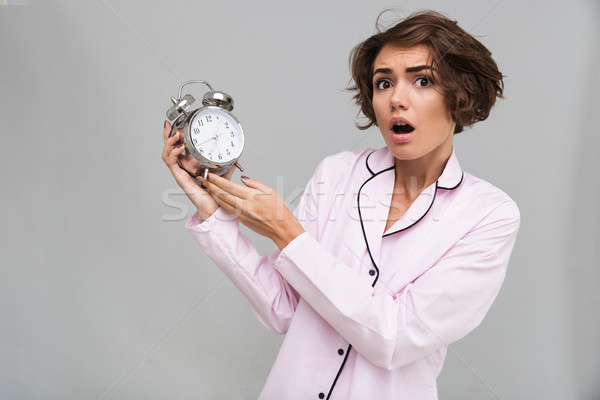 Portrait of a scared girl in pajamas holding alarm clock Stock photo © deandrobot