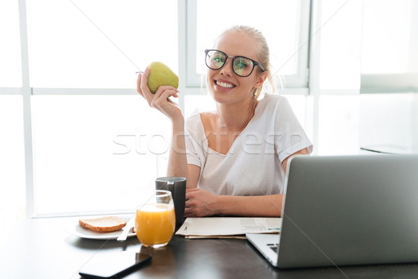 Cheerful lady with apple sitting in kitchen and looking camera Stock photo © deandrobot