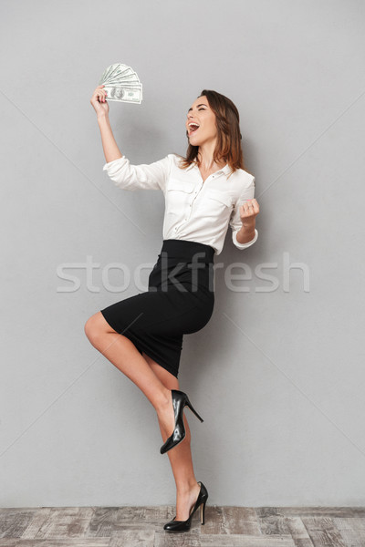 Excited young business woman make winner gesture holding money. Stock photo © deandrobot