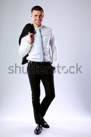Full length portrait of a happy business man holding jacket on shoulder on gray background Stock photo © deandrobot