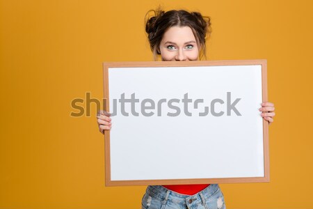 Smiling cute lovely young woman hiding behind blank board Stock photo © deandrobot