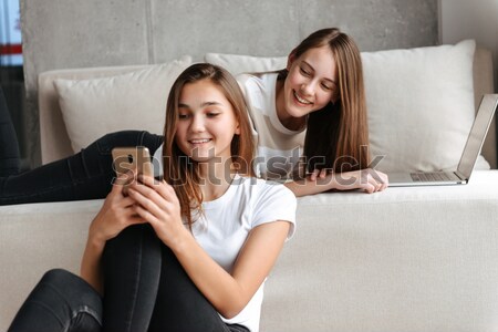 Two happy sisters twins lying on bed and reading magazine  Stock photo © deandrobot