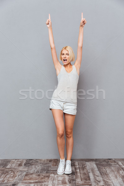 Happy beautiful young woman celebrating success and pointing up Stock photo © deandrobot