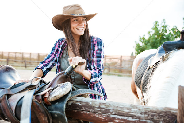 Happy woman cowgirl smiling and preparing saddle for riding horse Stock photo © deandrobot