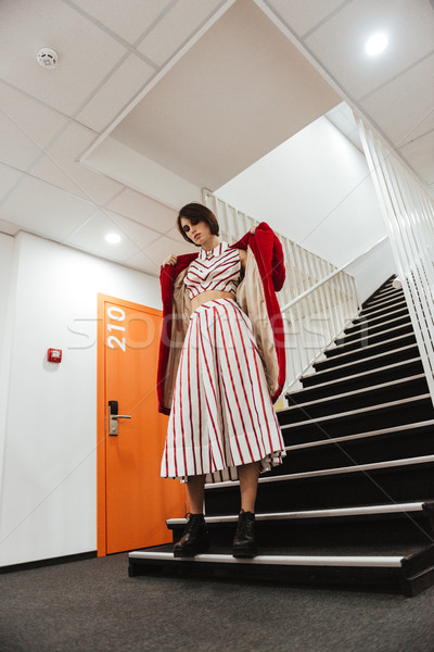 Beautiful young woman in red coat standing on stairs Stock photo © deandrobot