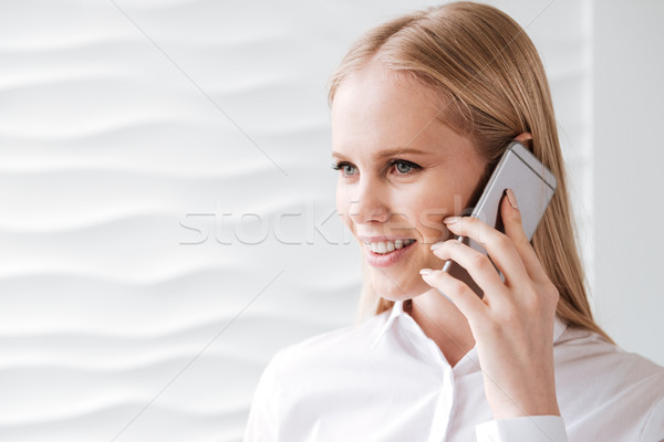 Stock photo: Cheerful young business woman in office talking by phone