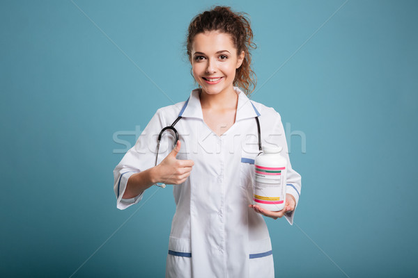 Female doctor holding bottle of pills and showing thumb up Stock photo © deandrobot