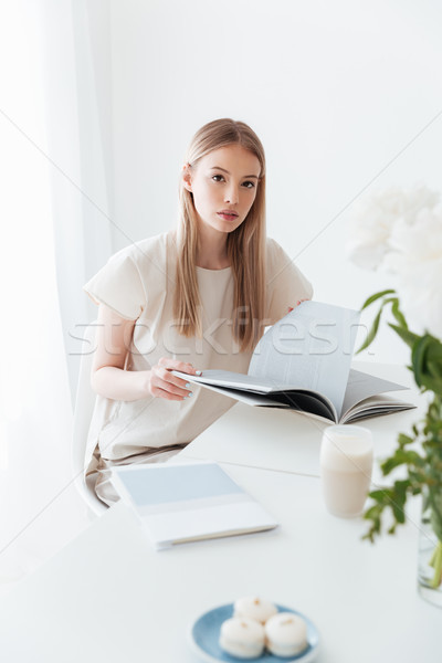 Woman sitting indoors reading book. Looking at camera. Stock photo © deandrobot