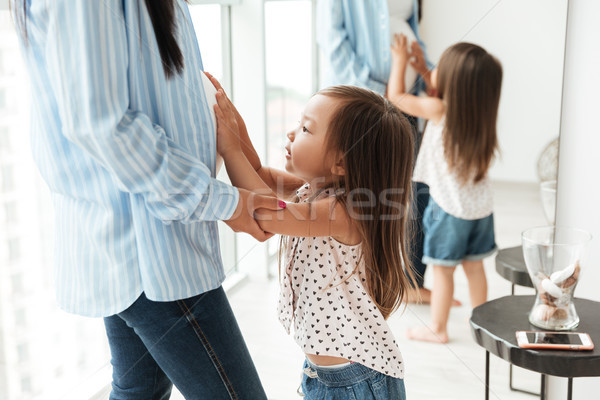 Cute little asian girl touching her pregnant mothers belly Stock photo © deandrobot