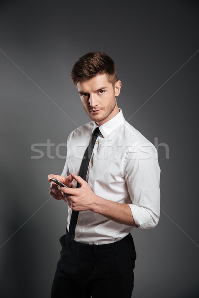 Businessman in formalwear holding mobile phone and looking at camera Stock photo © deandrobot