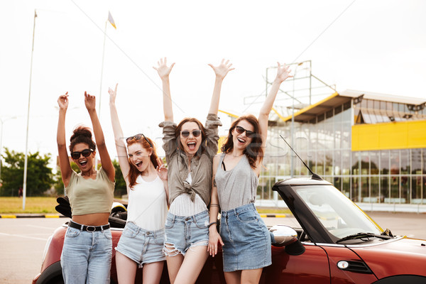 Four young women friends standing near car outdoors. Stock photo © deandrobot