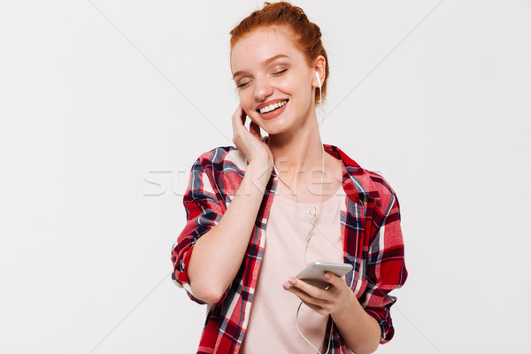 Pleased ginger woman in shirt and headphones listening music Stock photo © deandrobot