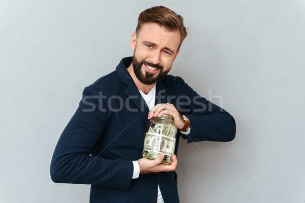 Concentrated smiling bearded man in business clothes trying opening jar Stock photo © deandrobot