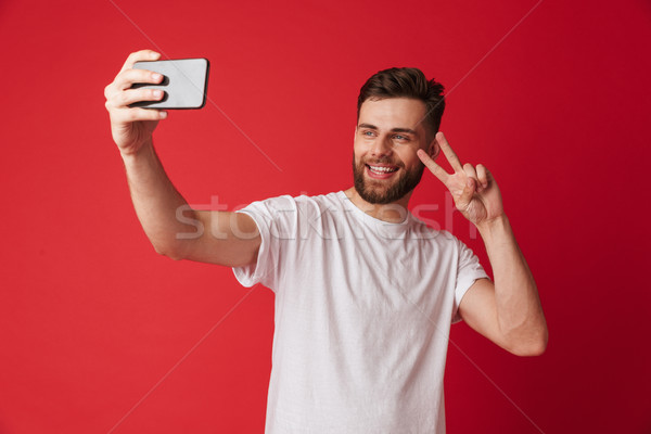 Young man standing isolated make selfie by mobile phone make peace gesture. Stock photo © deandrobot