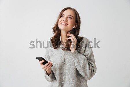 Pensive smiling brunette woman in sweater holding smartphone Stock photo © deandrobot