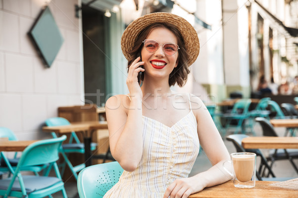 Pleased woman in dress and straw hat talking by smartphone Stock photo © deandrobot
